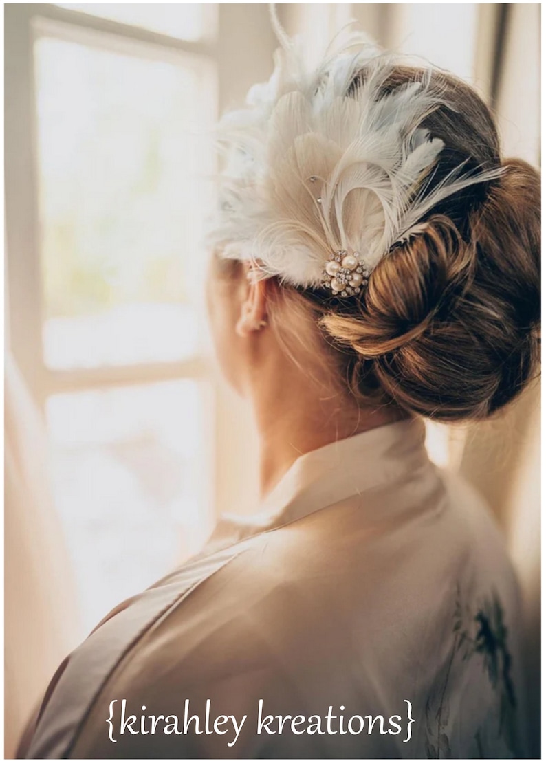 Puede incluir: Una mujer con un tocado de plumas blancas y un adorno de perlas y pedrer&iacute;a. El tocado se lleva en el pelo, que est&aacute; recogido en un mo&ntilde;o. La mujer lleva una bata blanca.