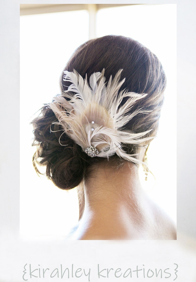 May include: A white feather hair comb with rhinestones. The comb is worn in a woman's hair, which is styled in a bun.