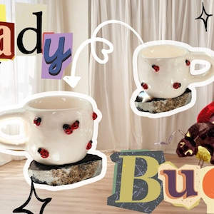 Puede incluir: Tazas de cerámica blanca decoradas con mariquitas rojas, colocadas sobre bases de piedra. Las palabras "Lady Bug" se muestran en un estilo collage con varias fuentes y colores. El fondo incluye una cortina y estrellas decorativas.