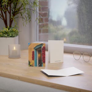 May include: Greeting cards featuring a photograph of a Southwestern-style door with red chili ristras. The cards are blank inside and have the photographer's name printed on the back. The cards are displayed on a wooden surface.