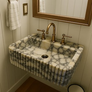 May include: A white marble bathroom sink with a fluted edge and a brass faucet with two handles. The sink is mounted on a white wall.