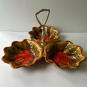 Può includere: Un vassoio da portata vintage a tre scomparti con manico dorato. Il piatto ha una forma a foglia con finitura smaltata marrone, gialla e rossa. Il manico è in metallo color oro.