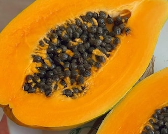 May include: A halved papaya with vibrant orange flesh and a cluster of dark, round seeds. The fruit's skin is a mix of green and yellow, indicating ripeness. The papaya is cut open, revealing its texture and color.