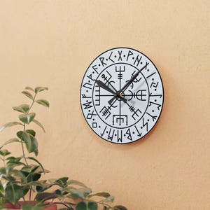 Puede incluir: Reloj redondo blanco con agujas negras y marcas negras. La esfera del reloj presenta un diseño de brújula con runas alrededor del borde. Las runas son en blanco y negro.