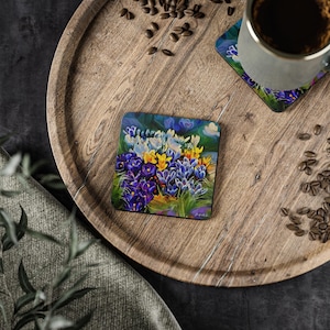 Könnte beinhalten: Ein quadratischer Untersetzer mit einem farbenfrohen Gemälde von lila, gelben und weißen Krokusblüten. Der Untersetzer ist aus Holz und hat eine natürliche Oberfläche.