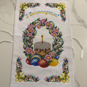 May include: White embroidered kitchen towel with a colourful Easter design. The design features a cake with a candle, Easter eggs, and flowers. The text "З Великоднем!" is embroidered in the centre of the towel.
