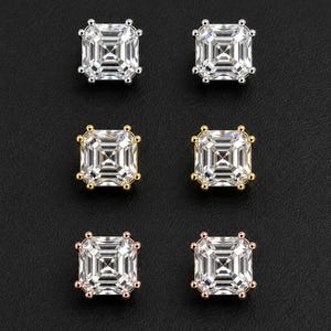 May include: Three pairs of square-cut stud earrings featuring clear, faceted stones set in silver, yellow gold, and rose gold metal prongs. Each earring has a four-prong setting that secures the square stone, creating a classic and symmetrical appearance.