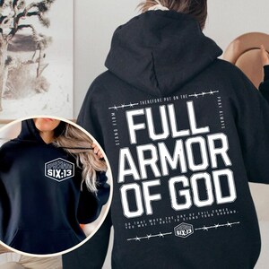May include: Black hoodie with the text "FULL ARMOR OF GOD" in large white letters on the back. The hoodie also features the text "SIX:13" and a small logo on the front. The hoodie has a hood and long sleeves.