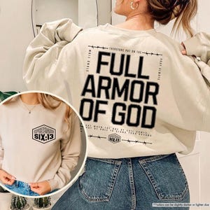 May include: Sand-colored sweatshirt with the text "FULL ARMOR OF GOD" in black on the back. The front of the sweatshirt features a smaller design with the text "SIX:13". The sweatshirt has long sleeves and a crew neck.