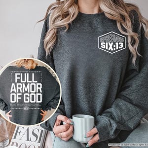 May include: Dark heather gray sweatshirt with the text "Ephesians Six:13" in a white hexagon on the chest. The back of the sweatshirt features the text "Full Armor of God" in a white rectangular design. A casual, comfortable style.