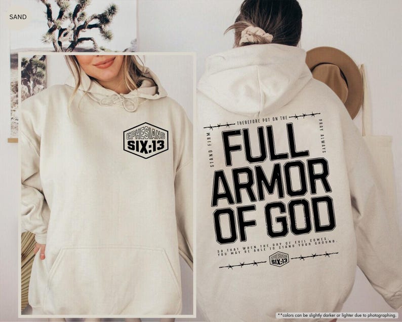 May include: Sand-colored hoodie with a front pocket and a hood. The front features a black and white hexagon graphic with the text "EPHESIANS SIX:13". The back displays "FULL ARMOR OF GOD" in bold black letters with additional text.