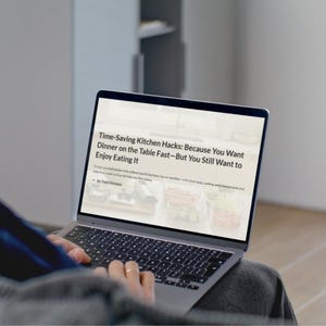 Puede incluir: Una persona usando una computadora portátil plateada. La pantalla muestra el texto "Time-Saving Kitchen Hacks: Because You Want Dinner on the Table Fast-But You Still Want to Enjoy Eating It". La computadora portátil está en el regazo de la persona.