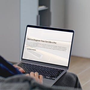 以下が含まれることがあります： 「How to Diagnose Your Car Like a Pro」というテキストが表示されたラップトップ。画面には車の診断に関するテキストと「by TRAIN HUMANS」というテキストが表示されています。ラップトップは開いており、人が使用しています。