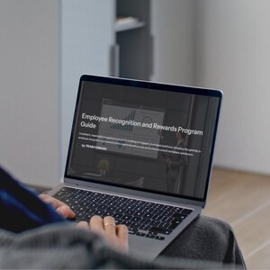 May include: A person using a laptop displaying a presentation titled "Employee Recognition and Rewards Program Guide." The screen shows a chart and text, with the words "by TRAIN HUMANS" at the bottom. The laptop is open on a person's lap.