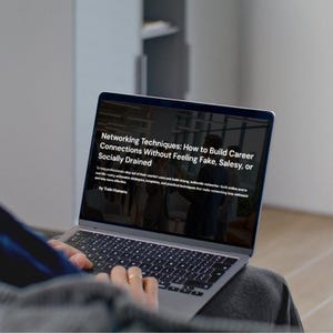 May include: A silver laptop displaying the text "Networking Techniques: How to Build Career Connections Without Feeling Fake, Salesy, or Socially Drained." The laptop is open, and the user's hands are visible on the keyboard.