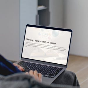 May include: A person using a laptop with the text "Writing Literary Analysis Essays" on the screen. The laptop is open, displaying text and graphics. The keyboard is visible, and the person's hands are on the keyboard.