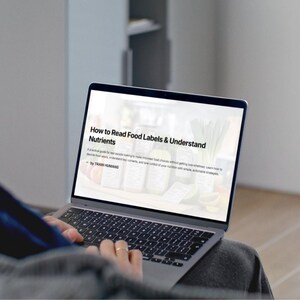 Könnte beinhalten: Ein Laptop-Bildschirm mit dem Text "How to Read Food Labels & Understand Nutrients". Der Bildschirm zeigt einen Leitfaden für fundierte Lebensmittelauswahl. Die Hände einer Person befinden sich auf der Tastatur des Laptops, der sich auf ihrem Schoß befindet.