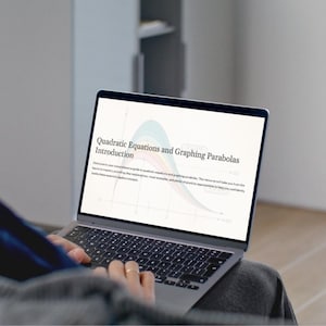 May include: A person using a laptop displaying a document titled "Quadratic Equations and Graphing Parabolas Introduction." The screen shows a graph with blue, green, and pink curves. The laptop is silver and has a black keyboard.