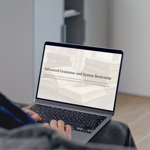 Könnte beinhalten: Ein Laptop mit dem Text "Advanced Grammar and Syntax Bootcamp" auf dem Bildschirm. Im Hintergrund sind Bücher zu sehen. Der Laptop ist geöffnet, die Hände des Benutzers sind auf der Tastatur zu sehen.