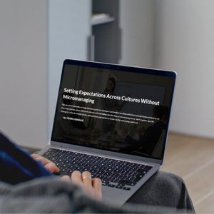 Pode incluir: Um laptop exibe o texto "Setting Expectations Across Cultures Without Micromanaging". A tela mostra uma apresentação com uma mulher falando. O laptop está no colo de uma pessoa.