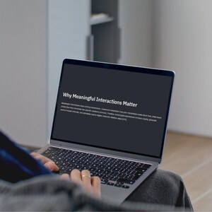 May include: A person using a silver laptop with the text "Why Meaningful Interactions Matter" on the screen. The laptop is open, displaying text on a dark background. The keyboard is visible, and the person's hands are on the keys.
