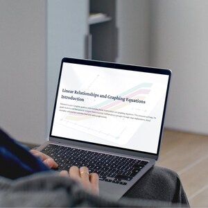 May include: A person using a laptop with the text "Linear Relationships and Graphing Equations Introduction" on the screen. The laptop is open, displaying a colorful graphic and text. The person is wearing a gray shirt.