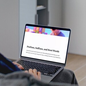 May include: A laptop screen shows a webpage titled "Prefixes, Suffixes, and Root Words." The screen displays colourful blocks and text about word structure. The laptop is open, with hands typing on the keyboard.