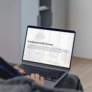 May include: A person using a laptop with the text "Introduction to MLA Format" on the screen. The laptop is open, displaying text and an illustration. The keyboard is visible, and the person's hands are on the keyboard.