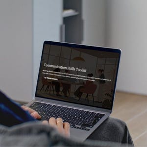 Op de afbeelding: Een persoon gebruikt een laptop met een presentatie getiteld "Communication Skills Toolkit". Het scherm toont een illustratie van mensen in een vergadering. De tekst op het scherm luidt ook "by TRAIN HUMANS."