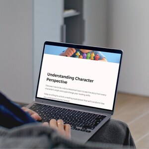 Op de afbeelding: Een laptop met een webpagina getiteld "Understanding Character Perspective". De pagina toont kleurrijke cartoonfiguren en tekst over het verbeteren van leesvaardigheid. De laptop staat open op de schoot van een persoon.