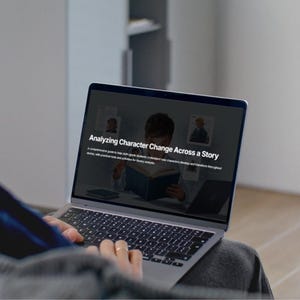 May include: A laptop displaying the title "Analyzing Character Change Across a Story." The screen shows a child reading a book, with additional images and text. The laptop is open, and the user's hands are visible on the keyboard.