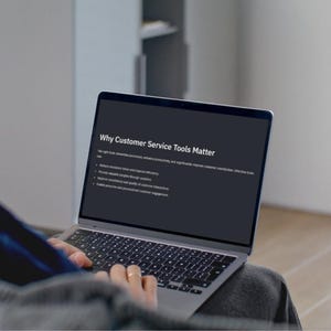 Peut inclure: Un ordinateur portable affiche le texte "Why Customer Service Tools Matter". L'écran présente une présentation avec des puces. La personne utilise l'ordinateur portable, portant un pull gris. L'ordinateur est sur ses genoux.