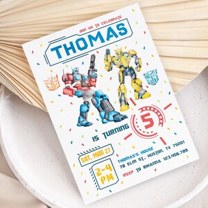 May include: A white invitation card with blue and red Transformers characters, confetti, and the text "THOMAS" and "5". The invitation includes the date, time, and RSVP information.