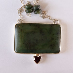 May include: A silver chain necklace with a rectangular green jade pendant and a small red gemstone hanging from the bottom.