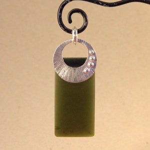 May include: A silver pendant with a textured circular design and small silver beads. The pendant is attached to a green stone rectangle.