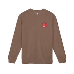 May include: Brown sweatshirt featuring a small red cartoon devil graphic on the chest. The devil is wearing a nappy and holding a small object. The sweatshirt has long sleeves and a crew neck.