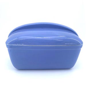 May include: A light blue, rectangular ceramic bread box with a curved handle on the lid. The box has a glossy finish and a thin white trim around the lid's edge. The design is simple and functional.