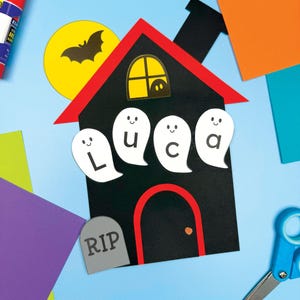 May include: A Halloween-themed craft project featuring a black house with a red roof and door. The house has a yellow moon with a bat, and ghost cutouts spelling "Luca". A gray tombstone with "RIP" is also included.