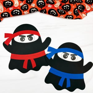 May include: Two black ninja ghost cutouts with red and blue headbands and sashes. The ghosts have white eyes and angry expressions. A Halloween-themed orange fabric with black pumpkin and ghost patterns is in the background.