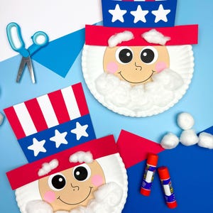 May include: Two Uncle Sam paper plate crafts with red, white, and blue patriotic hats and cotton wool beards. The crafts have smiling faces and are on a blue background. Scissors and glue sticks are also present.