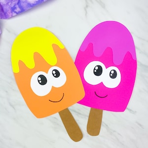 May include: Two colorful popsicle-shaped cutouts with smiling faces. One is orange with a yellow top, the other is pink. Both have brown popsicle sticks and large, cartoonish eyes. The background is a white marble pattern.