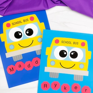 May include: Two rectangular posters featuring a yellow school bus illustration with large eyes and a smile. One poster has a dark blue background with the name Madd in red octagons. The other has a light blue background with the name Ryker in red octagons.