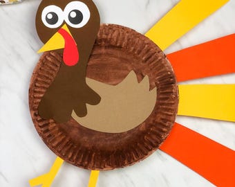Puede incluir: Una manualidad de pavo hecha a mano con un plato de papel marrón, cartulina marrón y beige, y tiras de papel naranja y amarillo de colores. El pavo tiene ojos saltones grandes, una carúncula roja y patas amarillas. Una divertida manualidad con temática de Acción de Gracias o otoño.