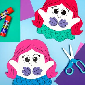 Könnte beinhalten: Zwei Meerjungfrau-Papierbastelarbeiten mit roten und rosa Haaren, weißen Gesichtern und blauen und grünen Schwänzen. Die Meerjungfrauen haben große Augen und sind von Bastelmaterialien umgeben, darunter Klebestifte und Scheren.