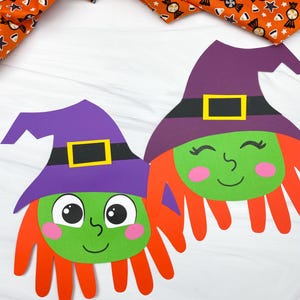 May include: Two Halloween witch-themed paper crafts. Each witch has a green face, orange hair, and a purple hat with a black band and a yellow buckle. The background includes orange fabric with candy and star patterns.