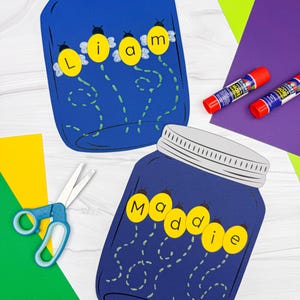 May include: Two blue mason jar cutouts with silver lids, each featuring a name spelled out with yellow firefly-shaped letters. One jar says "Liam" and the other says "Maddie". Craft supplies like scissors, glue sticks, and colored paper are scattered around.