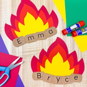 Può includere: Due ritagli di carta a forma di falò con i nomi "Emma" e "Bryce" su ritagli di tronchi di legno. Le fiamme sono a strati rosse, arancioni e gialle. Forbici e stick di colla sullo sfondo, insieme a carta colorata.