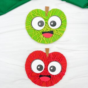 May include: Two apple-shaped crafts, one green and one red, each with a smiling face. The apples are made with yarn wrapped around a heart-shaped base. The green apple has a brown stem, and the red apple also has a brown stem. The eyes are large and white with black pupils.