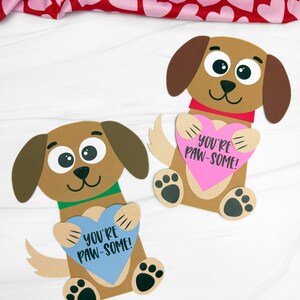 Op de afbeelding: Twee bruine papieren hondenuitsparingen met grote ogen en floppy oren, elk met een hartvormig bord. Eén bord is blauw en de andere roze, beide met de tekst "YOU'RE PAW-SOME!" De honden hebben zwarte pootafdrukken.