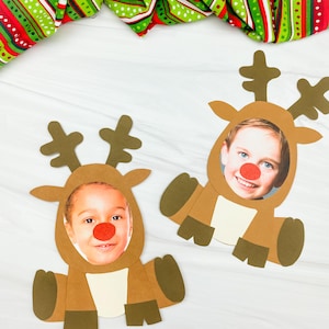 May include: Two reindeer-themed photo cutouts featuring children's faces and red noses. The reindeer are brown with tan bellies and antlers. A festive red, green, and white striped fabric is in the background. Ideal for Christmas crafts or holiday decorations.